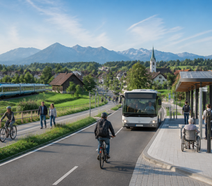 Eine malerische Landschaft mit Bergen im Hintergrund. Auf der Straße fahren ein Bus und ein Zug. Menschen nutzen Fahrräder, während andere an einer Haltestelle sitzen oder stehen. Die Umgebung ist grün und bietet eine angenehme Atmosphäre.