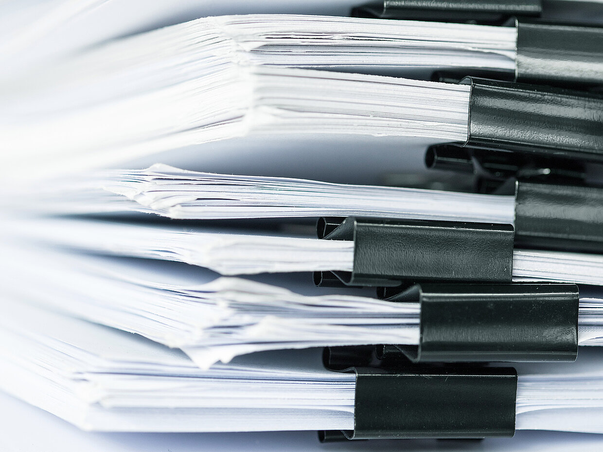 Nahaufnahme von mehreren gehefteten Papierstapeln, die mit schwarzen Büroklammern zusammengehalten werden. Die Dokumente sind gestapelt und zeigen teilweise weiße Ränder.