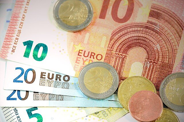 Ein Haufen Euro-Banknoten und -Münzen. Sichtbar sind ein 10-Euro-Schein, ein 20-Euro-Schein sowie mehrere Münzen in verschiedenen Werten, darunter eine 2-Euro-Münze und eine 1-Cent-Münze.