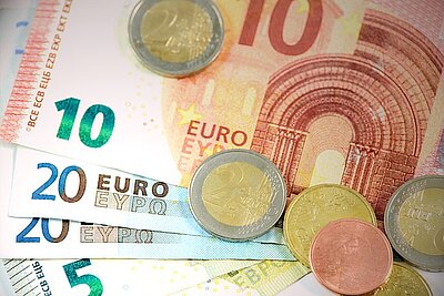 Ein Haufen Euro-Banknoten und -Münzen. Zu sehen sind Scheine in den Nennwerten 5, 10 und 20 Euro sowie verschiedene Euro-Münzen.