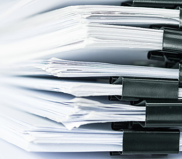 Nahaufnahme von mehreren gehefteten Papierstapeln, die mit schwarzen Büroklammern zusammengehalten werden. Die Dokumente sind gestapelt und zeigen teilweise weiße Ränder.
