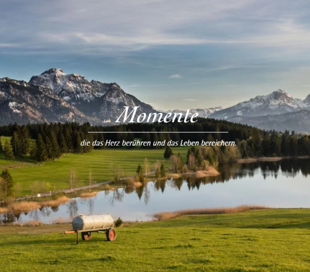 © Tourismusverband Ostallgäu e.V. Ein malerischer Ausblick auf einen See, umgeben von grünen Wiesen und Bergen. Im Vordergrund steht ein Holzfass auf einem Wagen. Rechts ist eine kleine, weiße Kapelle mit rotem Dach zu sehen. Der Himmel ist klar mit wenigen Wolken. Text: "Momente, die das Herz berühren und das Leben bereichern.