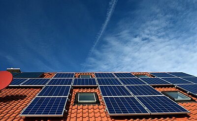 Ein Dach mit mehreren Solarpanels, die in Reihen angeordnet sind, unter einem klaren blauen Himmel. Die Dachziegel sind rot.