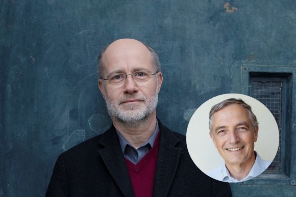 Ein älterer Mann mit Brille und kurzem, grauem Haar steht vor einer blauen Wand. Er trägt einen schwarzen Mantel über einem roten Pullover. In der rechten oberen Ecke ist ein kreisrundes Bild eines lächelnden Mannes mit grauen Haaren und heller Kleidung.
