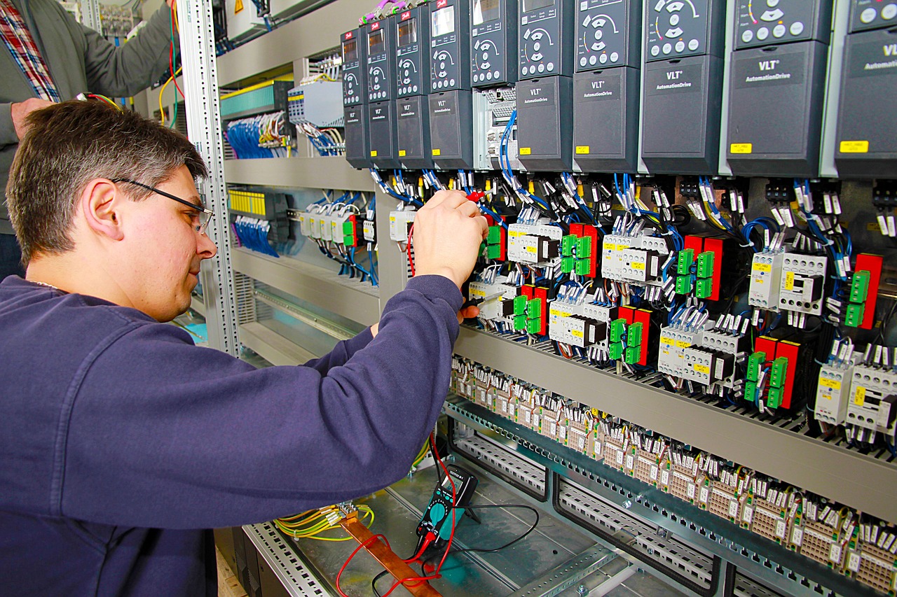 Ein Techniker repariert oder wartet ein Steuerungssystem in einem Schaltschrank. Er konzentriert sich auf die Verdrahtung und den Anschluss von elektrischen Komponenten. Im Hintergrund sind weitere elektronische Geräte und Kabel zu sehen.